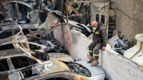 رجل إطفاء يجلس على حائط منخفض بجوار سيارات محترقة، في موقع دمار بعد غارة جوية في بيروت، مع آثار الدخان والحطام حوله.