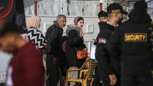 مجموعة فلسطينية تنتظر أمام مبنى في غزة وسط تواجد أفراد أمن، تعكس الأوضاع اليومية والتحديات الحياتية في ظل الاحتلال.