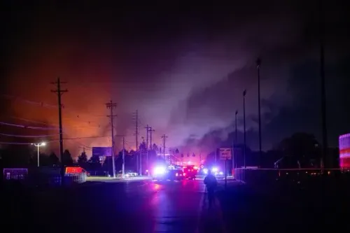 أضواء الطوارئ تضيء في لويزفيل بعد تحطم طائرة شحن UPS، مع تصاعد الدخان وألسنة اللهب في الخلفية، مما يعكس حجم الكارثة.