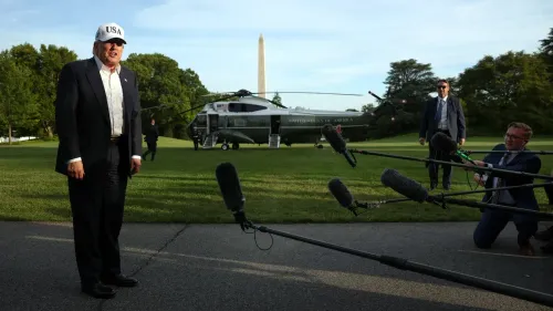 ترامب يرتدي قبعة مكتوب عليها "USA" ويتحدث إلى الصحفيين في حديقة البيت الأبيض، مع وجود مروحية خلفه ونصب واشنطن في الخلفية.