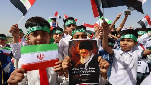 أطفال يحملون أعلام إيران والعراق، ويظهرون لافتة تحمل صورة قائد إيراني، خلال مظاهرة لدعم المقاومة في المنطقة.