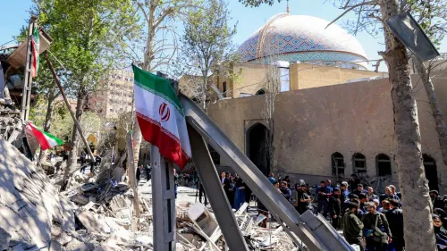 دمار كبير في جامعة إيرانية بعد الضربات الإسرائيلية، مع وجود علم إيران بين الأنقاض وأشخاص يتجمعون في الموقع.