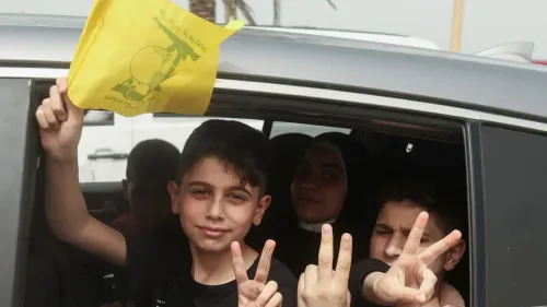 طفل يحمل علم حزب الله الأصفر من نافذة سيارة، مبتسمًا ويظهر علامة النصر، بينما يظهر آخرون في الخلفية. تعكس الصورة أجواء الدعم والتأييد.