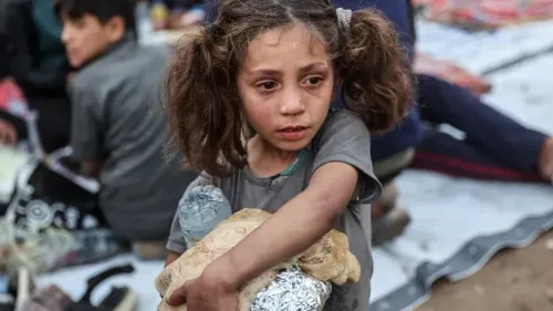 طفلة صغيرة تحمل خبزًا وزجاجة ماء، تعبر عن معاناة الأطفال في غزة وسط الدمار، تعكس واقع الحرب والجوع.