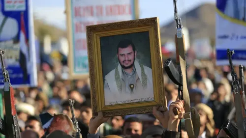 محتجون يحملون صورة مؤطرة لزعيم الحوثيين، مع وجود أسلحة في الخلفية، خلال تظاهرة دعم لإيران والجبهات المقاومة.