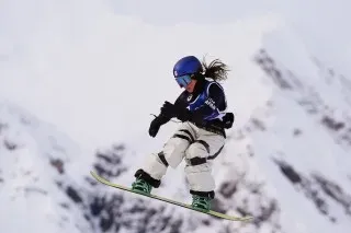 متزلجة تتحدى الجاذبية أثناء قفزها على لوح التزلج في جبال الألب الإيطالية، تعكس روح المنافسة في دورة الألعاب الأولمبية.