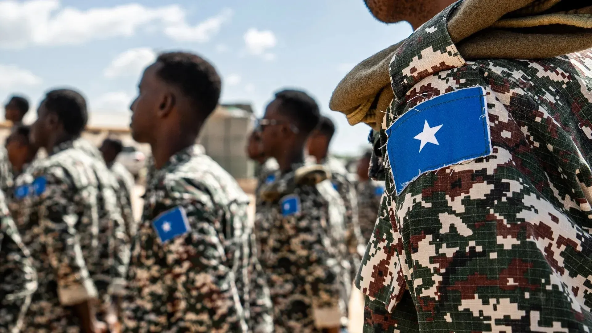 جنود من الجيش الصومالي يرتدون زيًا عسكريًا مموهًا مع شارة العلم الوطني، أثناء تجمع في موقع عسكري.