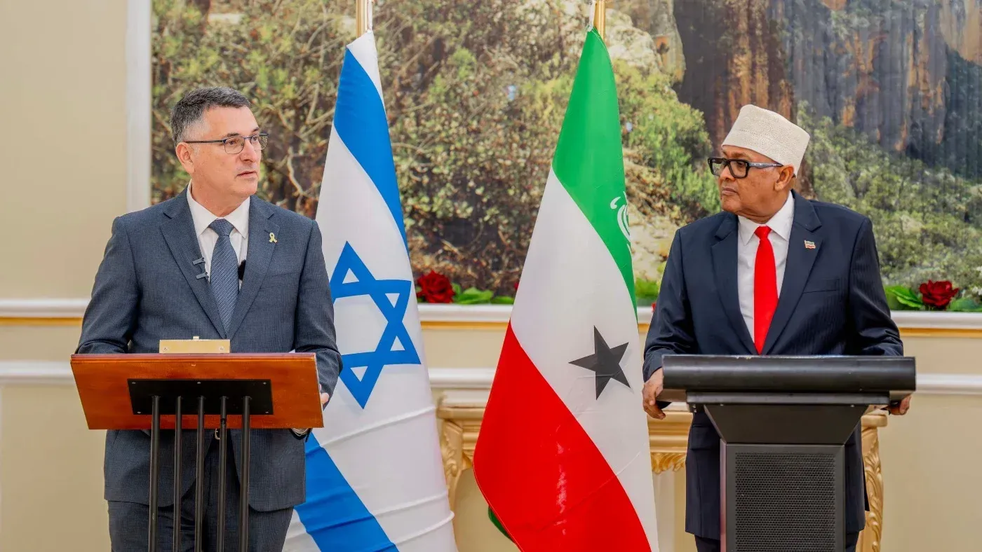 اجتماع بين مسؤول إسرائيلي ورئيس إقليم أرض الصومال، مع العلمين الإسرائيلي والأخضر والأحمر لأرض الصومال في الخلفية، يناقشان التعاون الاستثماري.