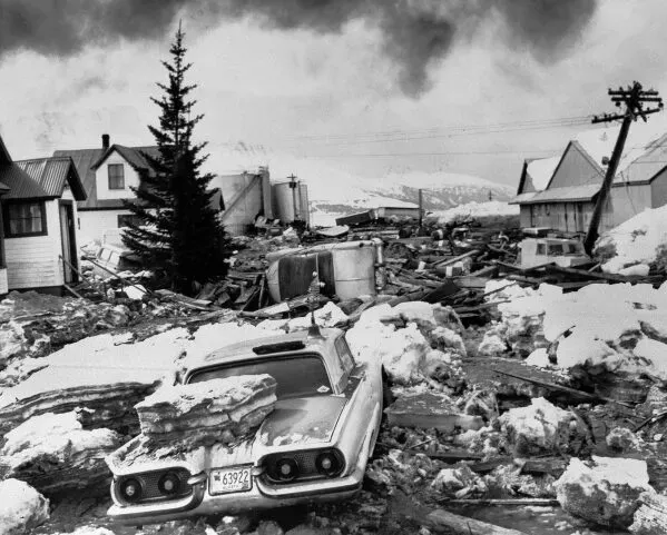 صورة تاريخية تظهر آثار زلزال ألاسكا عام 1964، مع سيارة مدمرة ومنازل مدمرة وسط الفوضى والثلوج.