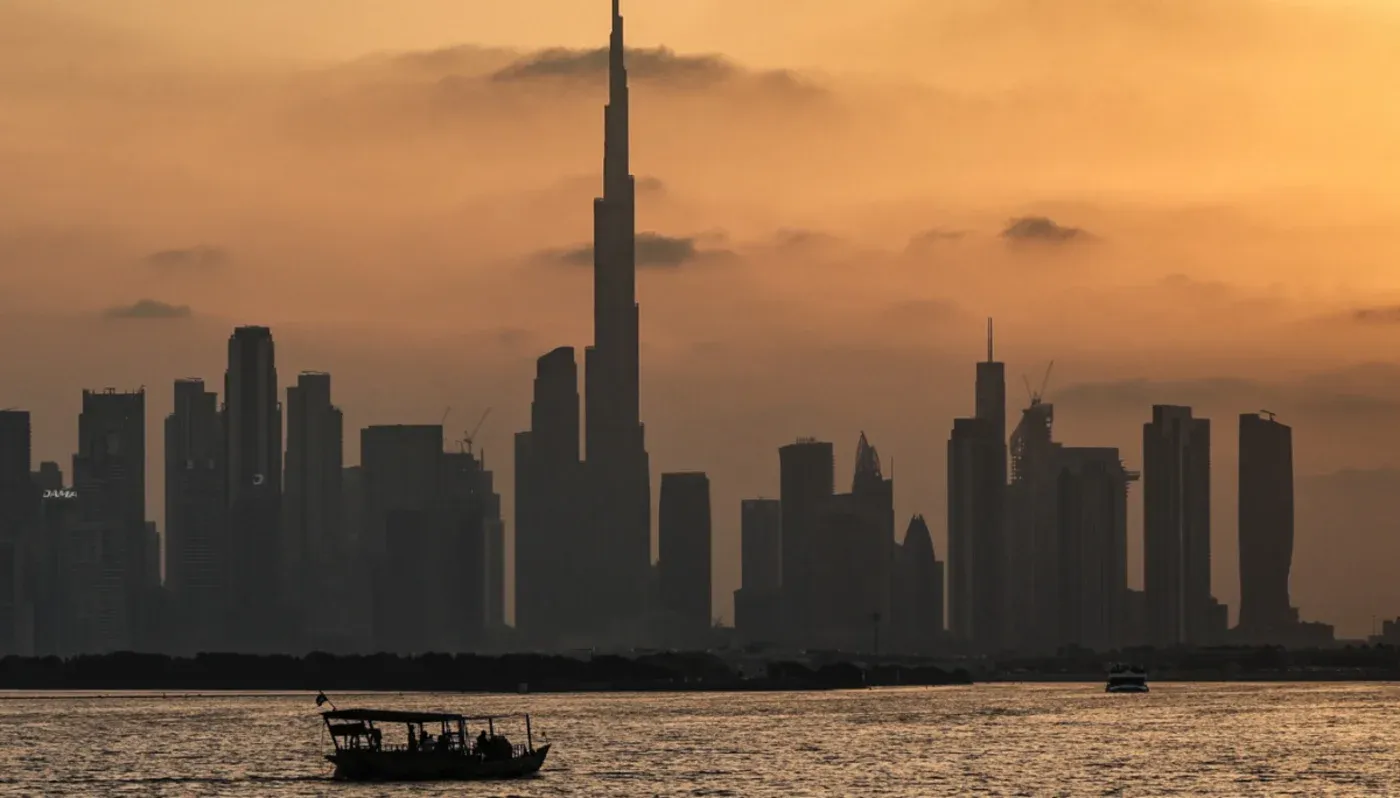 غروب الشمس خلف برج خليفة في دبي، مع قارب صغير يبحر في المياه، يعكس التحديات التي تواجه قطاع الشحن في ظل الأزمات الحالية.