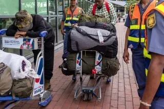 وصول مجموعة من المواطنين الجنوب أفريقيين إلى مطار، يحملون أمتعتهم بعد عودتهم من أوكرانيا، مع تعبيرات وجه تعكس الإرهاق والقلق.