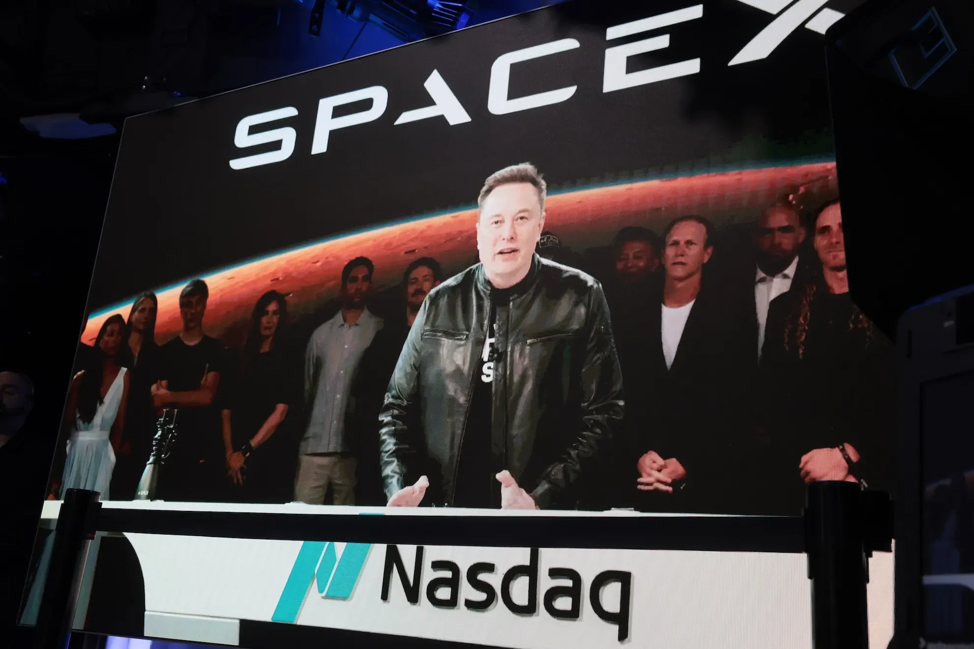إيلون ماسك يتحدث في حدث لشركة SpaceX أمام شعار Nasdaq، مع التركيز على نمو إيرادات الذكاء الاصطناعي وتوسع الشركة في البنية التحتية.