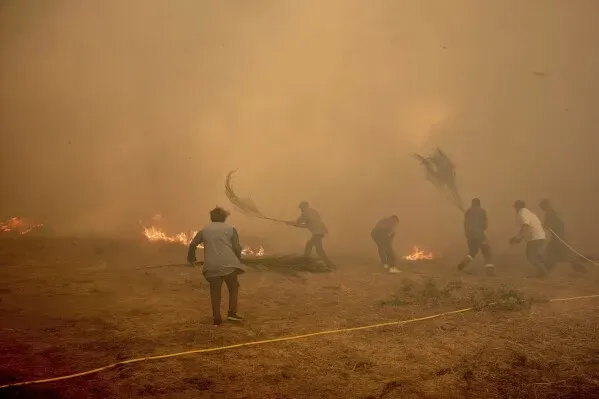 أشخاص محليين يحاولون إخماد حرائق الغابات في إسبانيا باستخدام أدوات بسيطة، وسط دخان كثيف وظروف خطرة.