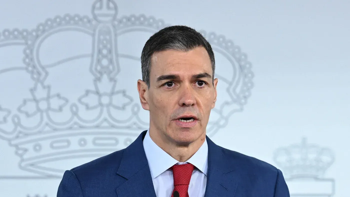 رئيس الوزراء الإسباني بيدرو سانشيز يتحدث في مؤتمر صحفي، مع خلفية تحمل رموزًا ملكية، معبرًا عن موقف إسبانيا ضد الحرب.