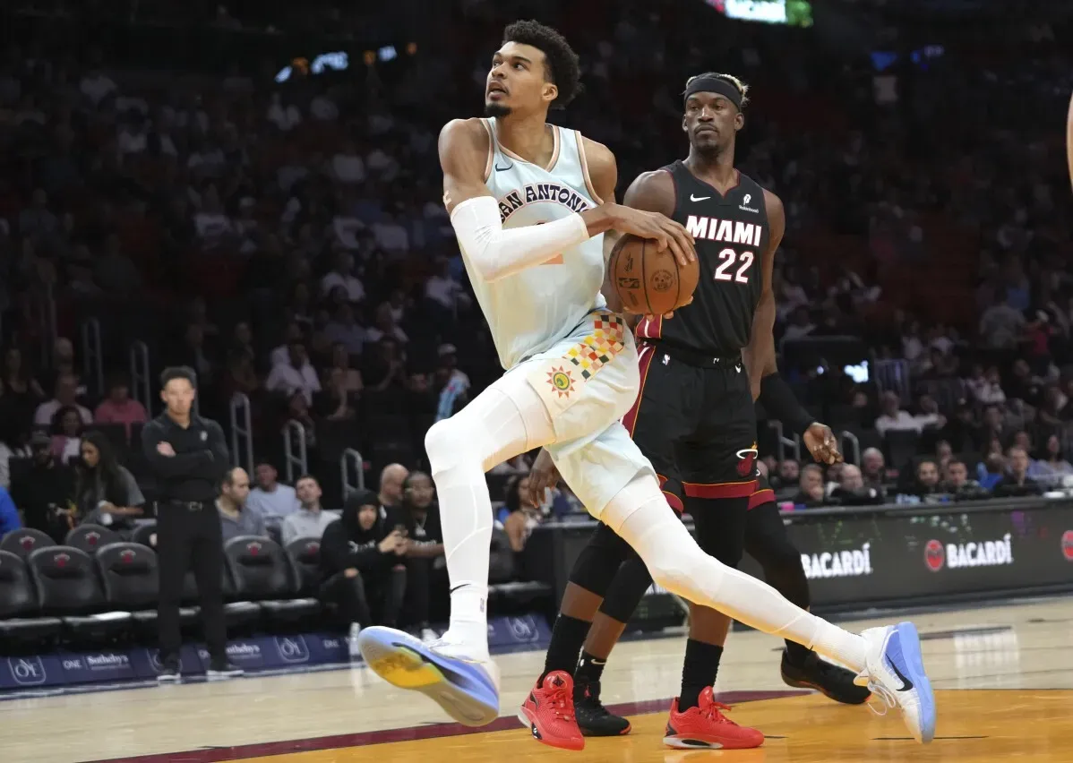 في الصورة، لاعب كرة السلة فيكتور ويمبانياما من فريق سان أنطونيو يقوم برمية خلال مباراة في دوري NBA، بينما يتابع خصمه من فريق ميامي.