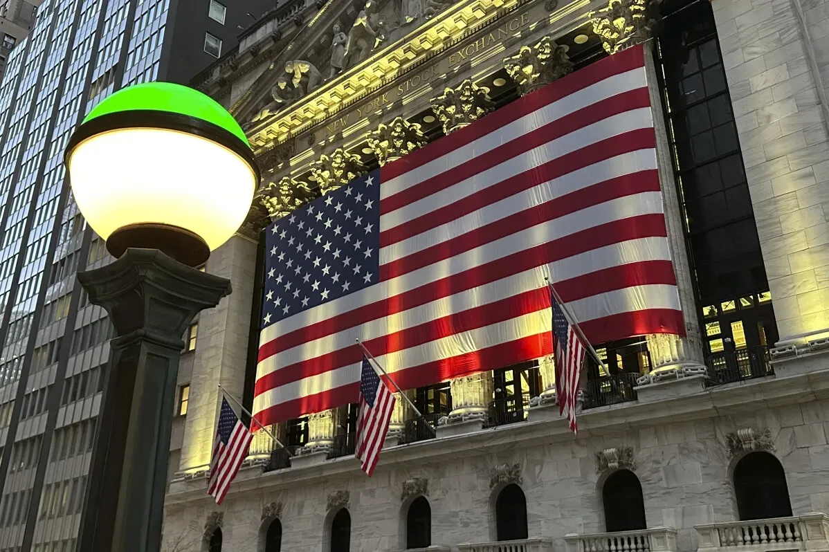علم الولايات المتحدة يزين واجهة بورصة نيويورك، مع مصباح شوارع مضاء في المقدمة، مما يعكس النشاط المالي في المدينة.