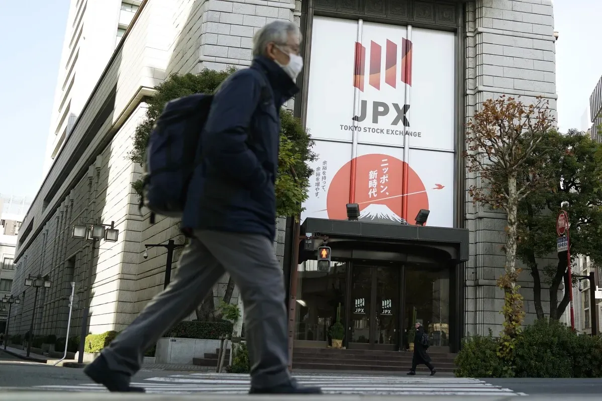 مشاة يمرون أمام مبنى بورصة طوكيو، مع لافتة تحمل شعار JPX وصورة لجبل فوجي، في سياق تداول الأسهم الآسيوية.