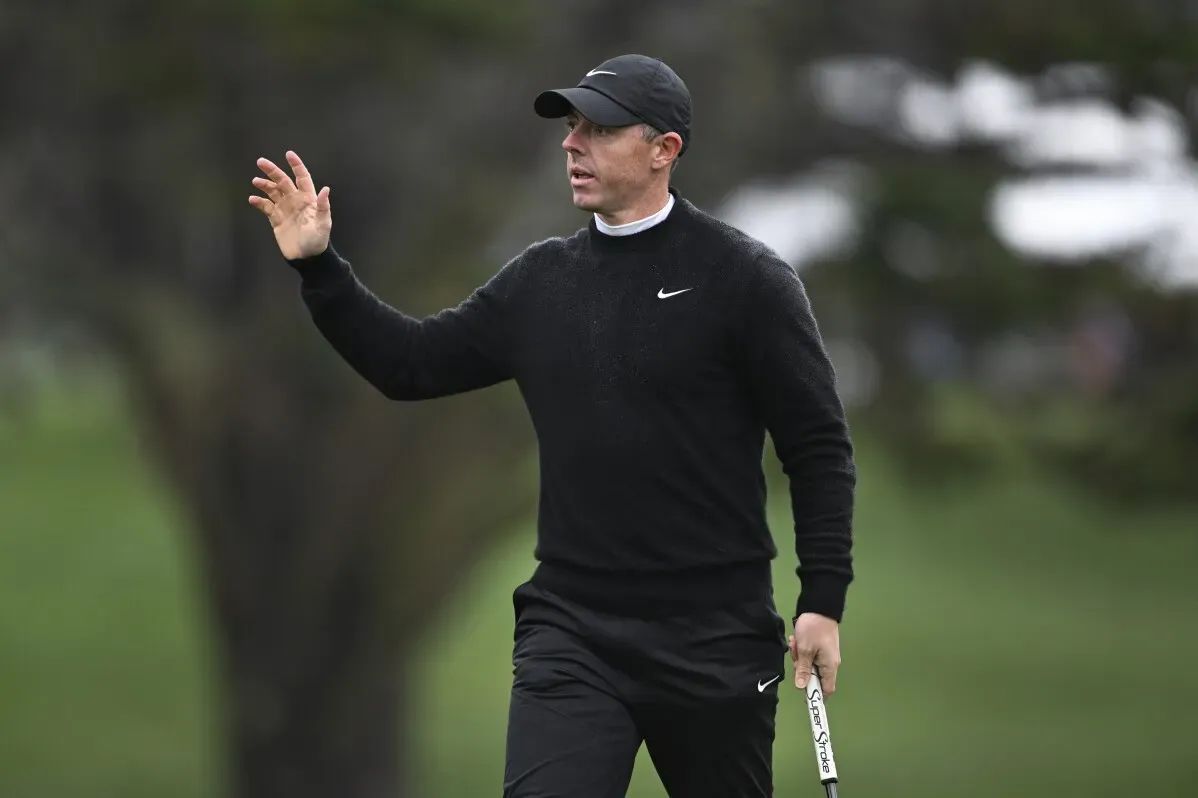 لاعب الجولف روري ماكلروي يرتدي ملابس سوداء، يلوح بيده أثناء الجولة في بطولة AT&T Pebble Beach Pro-Am، مع خلفية طبيعية.
