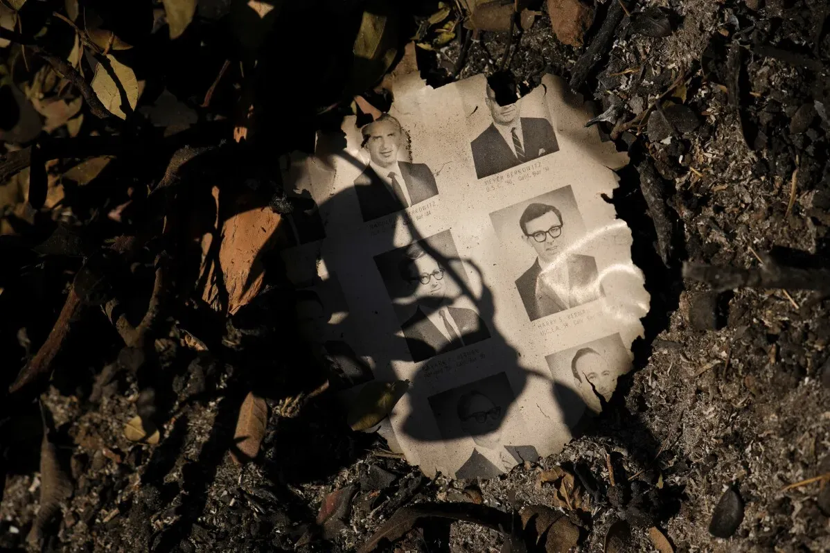 صورة ورقة محترقة تظهر صوراً لأشخاص، محاطة بأوراق محترقة وأرضية سوداء، تعكس آثار حرائق الغابات في كاليفورنيا.