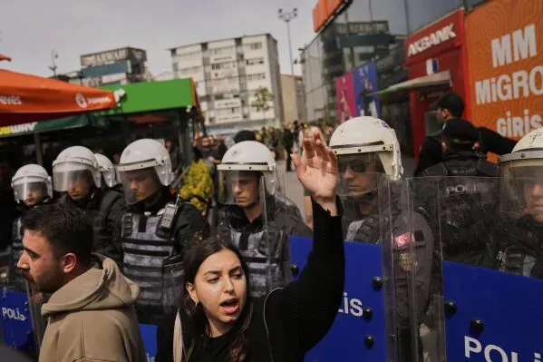 محتجون في إسطنبول يواجهون الشرطة خلال مظاهرة ضد الحكومة، مع ظهور عناصر الأمن في الخلفية. تعكس الصورة التوترات السياسية الحالية.