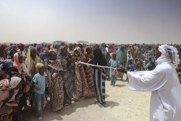 حشود من اللاجئين السودانيين في مخيم أدره بتشاد، مع وجود رجل يوزع المساعدات. تعكس الصورة تحديات النزوح بسبب الحرب الأهلية.