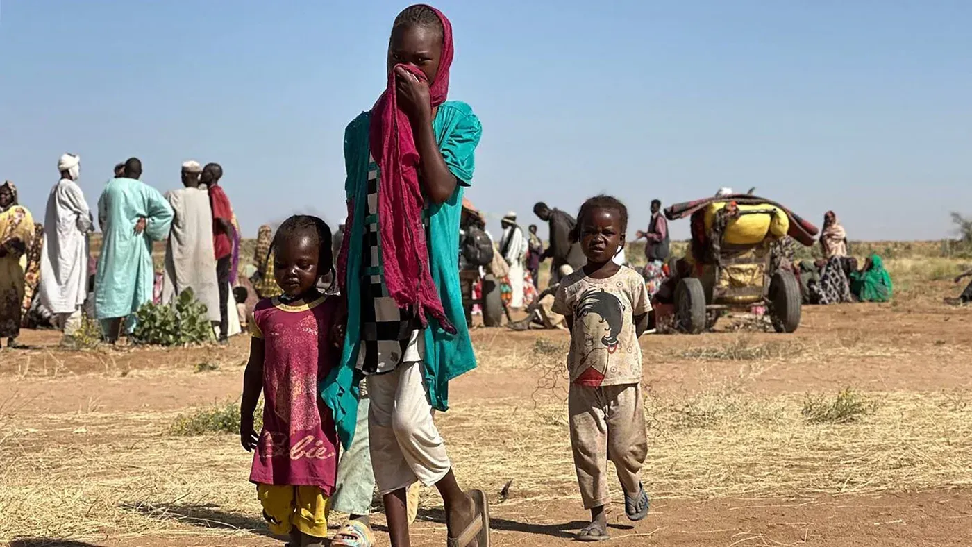 أطفال من طائفة المساليت في السودان يقفون في منطقة نازحين، مع خلفية لأشخاص آخرين، وسط أوضاع إنسانية صعبة.