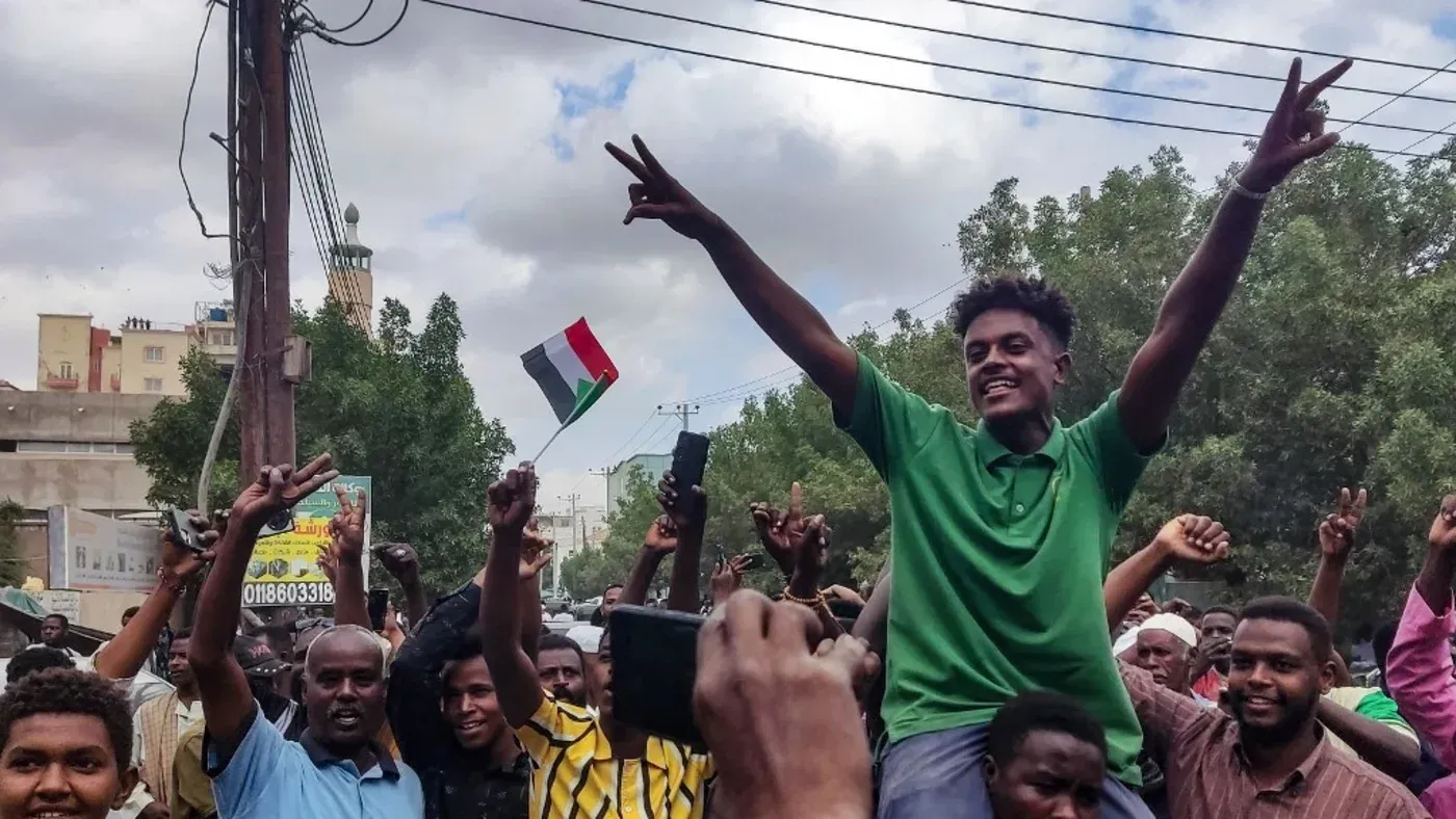 محتجون في ود مدني يحتفلون بعد استعادة الجيش السيطرة على المدينة، حاملين الأعلام ويظهرون علامات النصر.