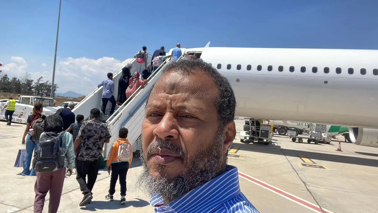 رجل أعمال سوداني-هولندي يقف أمام طائرة، مع مجموعة من الأشخاص يصعدون إليها، بعد إطلاق سراحه من الاحتجاز في السودان.