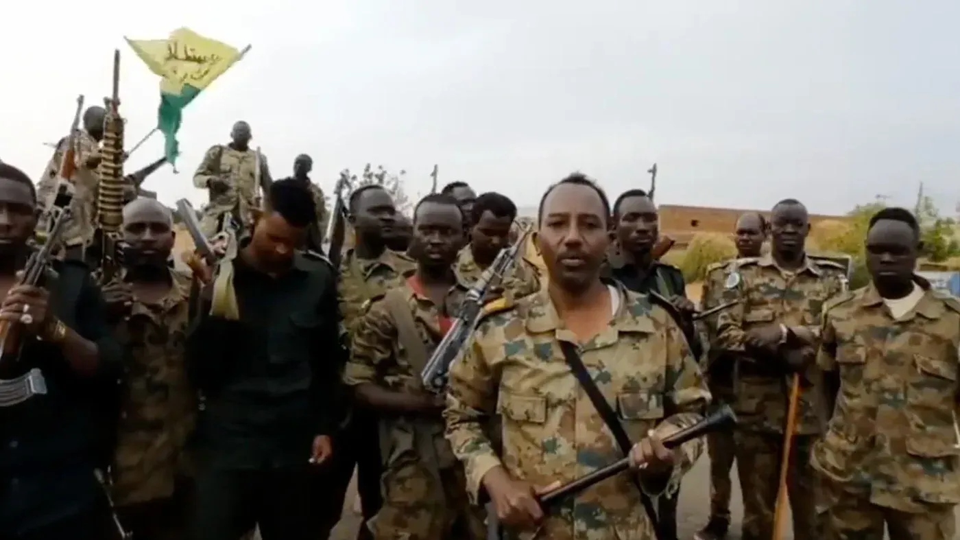 جنود من الجيش السوداني في مدينة الأبيض، يحملون أسلحة، مع علم يرمز إلى القوات. يعكس المشهد الأوضاع المتوترة في المنطقة.