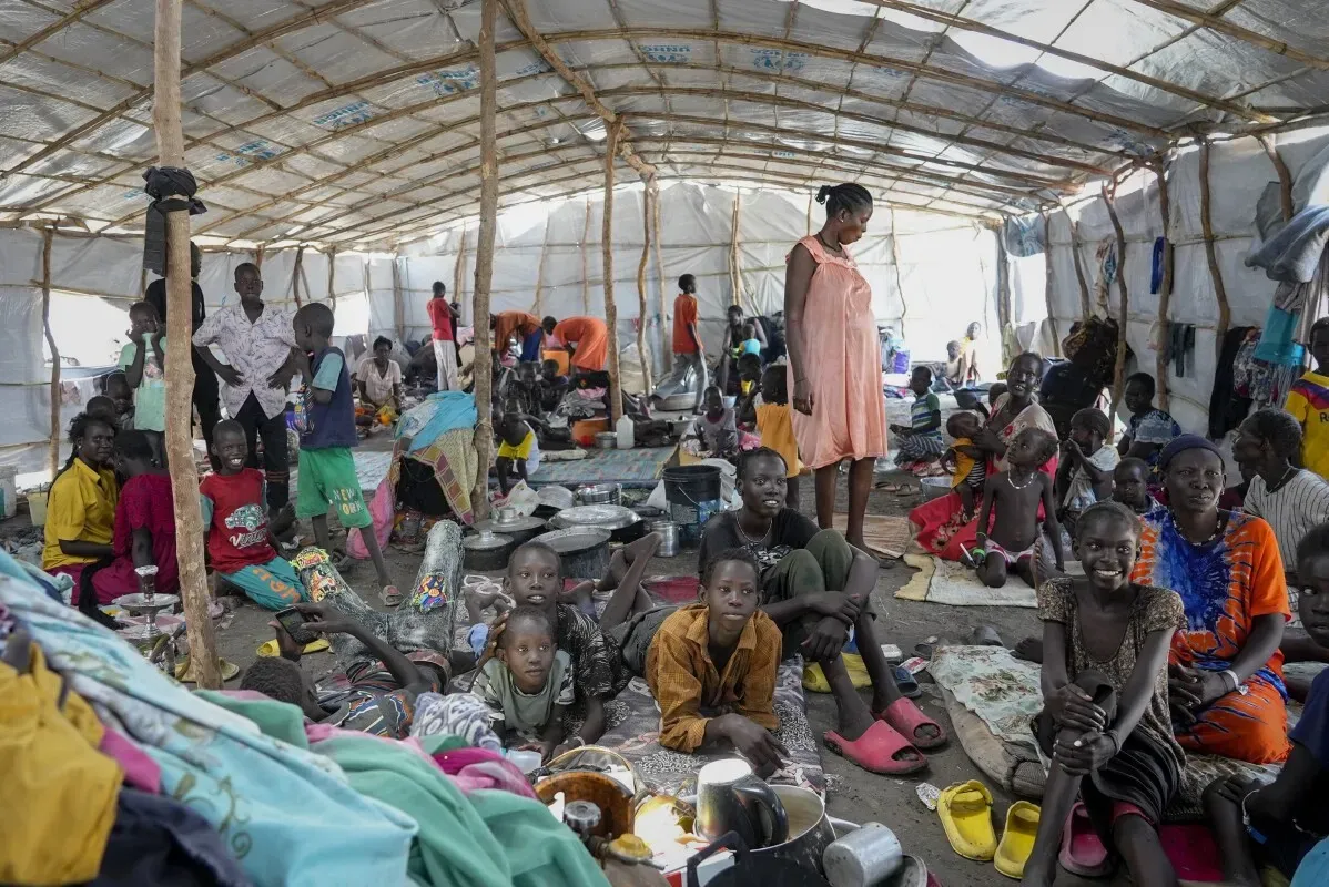 لاجئون في مخيم مؤقت في السودان، يعكسون معاناة النزوح بسبب الحرب. يظهر الأطفال والنساء في بيئة مكتظة، مما يبرز الأزمة الإنسانية المستمرة.