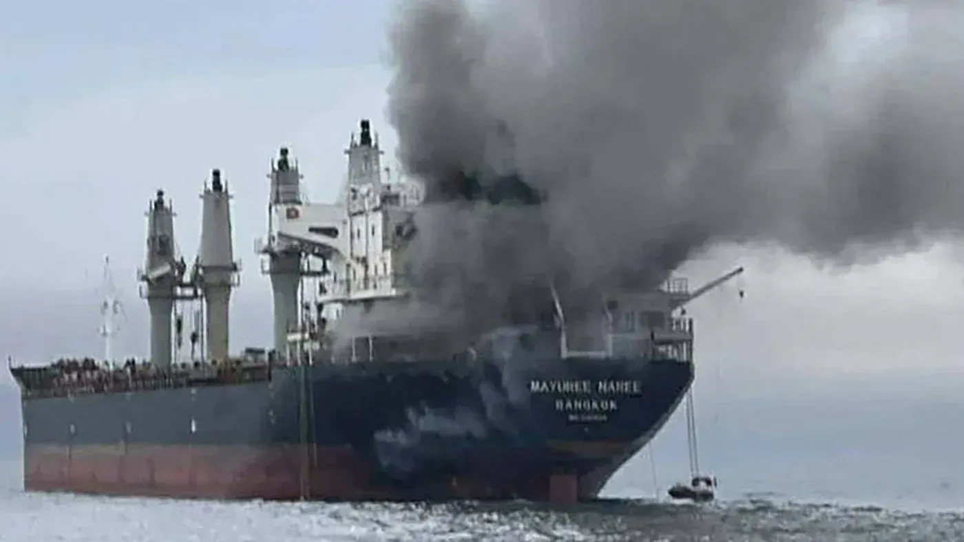 سفينة تجارية تتصاعد منها أعمدة من الدخان في البحر، مما يشير إلى هجوم إيراني في مضيق هرمز وسط تصاعد التوترات الإقليمية.