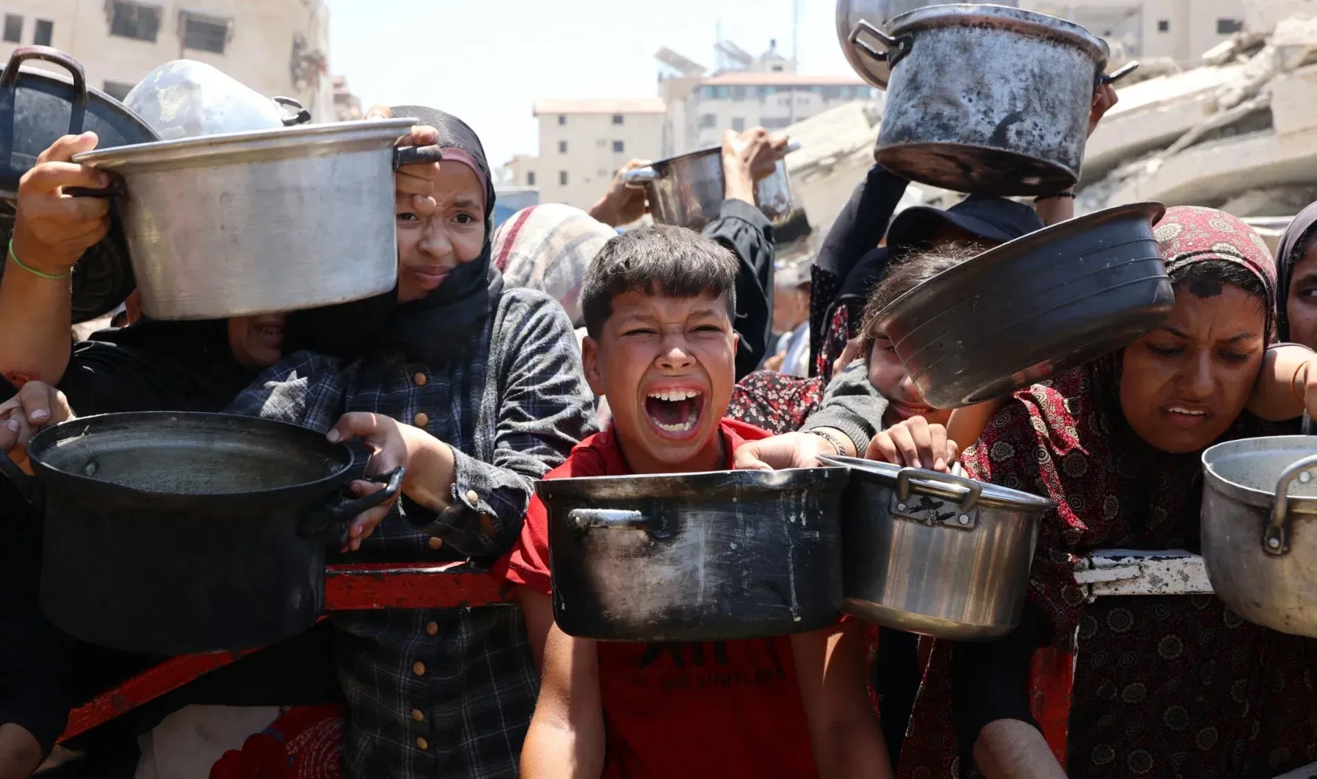 أطفال ونساء فلسطينيون يصرخون في طابور للحصول على المساعدات الغذائية في غزة، مع تزايد الأوضاع الإنسانية الصعبة.