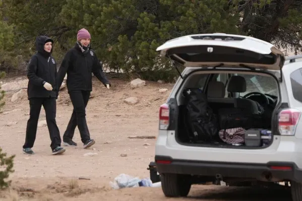 عناصر من الشرطة تسير في منطقة ريفية بالقرب من سيارة SUV مفتوحة، حيث يُجري المحققون بحثًا عن أدلة في قضية قتل ثلاث نساء في يوتا.