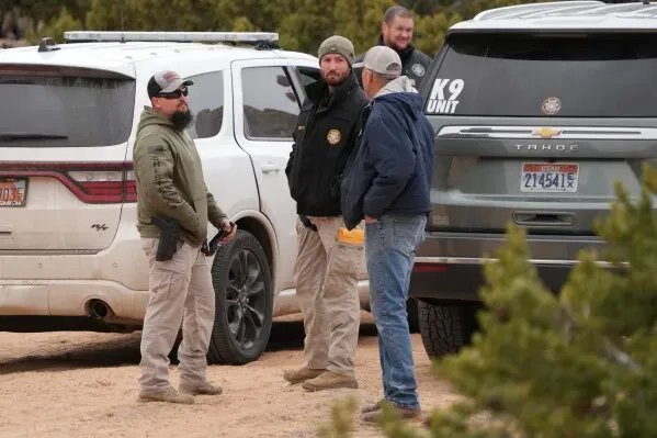 رجال الشرطة يتحدثون في منطقة صحراوية في يوتا، مع وجود سيارات دورية خلفهم، في سياق تحقيق يتعلق بجرائم قتل.