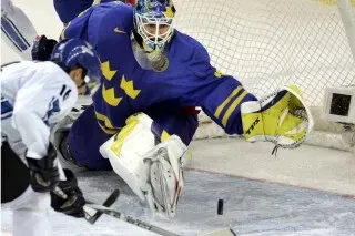 حارس مرمى سويدي يتصدى لقرص هوكي خلال مباراة، مع وجود لاعب فنلندي في المقدمة، في سياق المنافسة الأولمبية بين السويد وفنلندا.