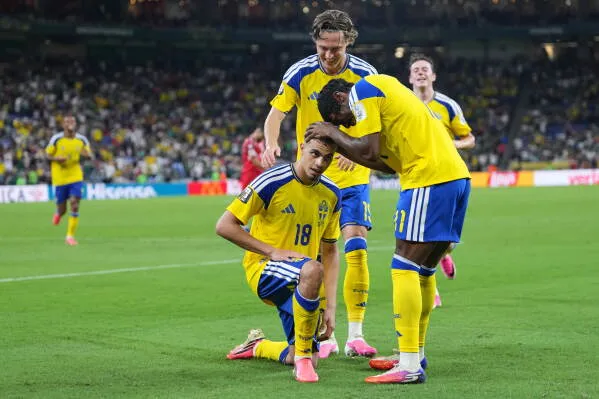 ياسين أياري يحتفل بتسجيل هدفه الثاني في مباراة السويد ضد تونس بكأس العالم، محاطًا بزملائه، مع إيماءة تعبيرية تعكس انتماءه.
