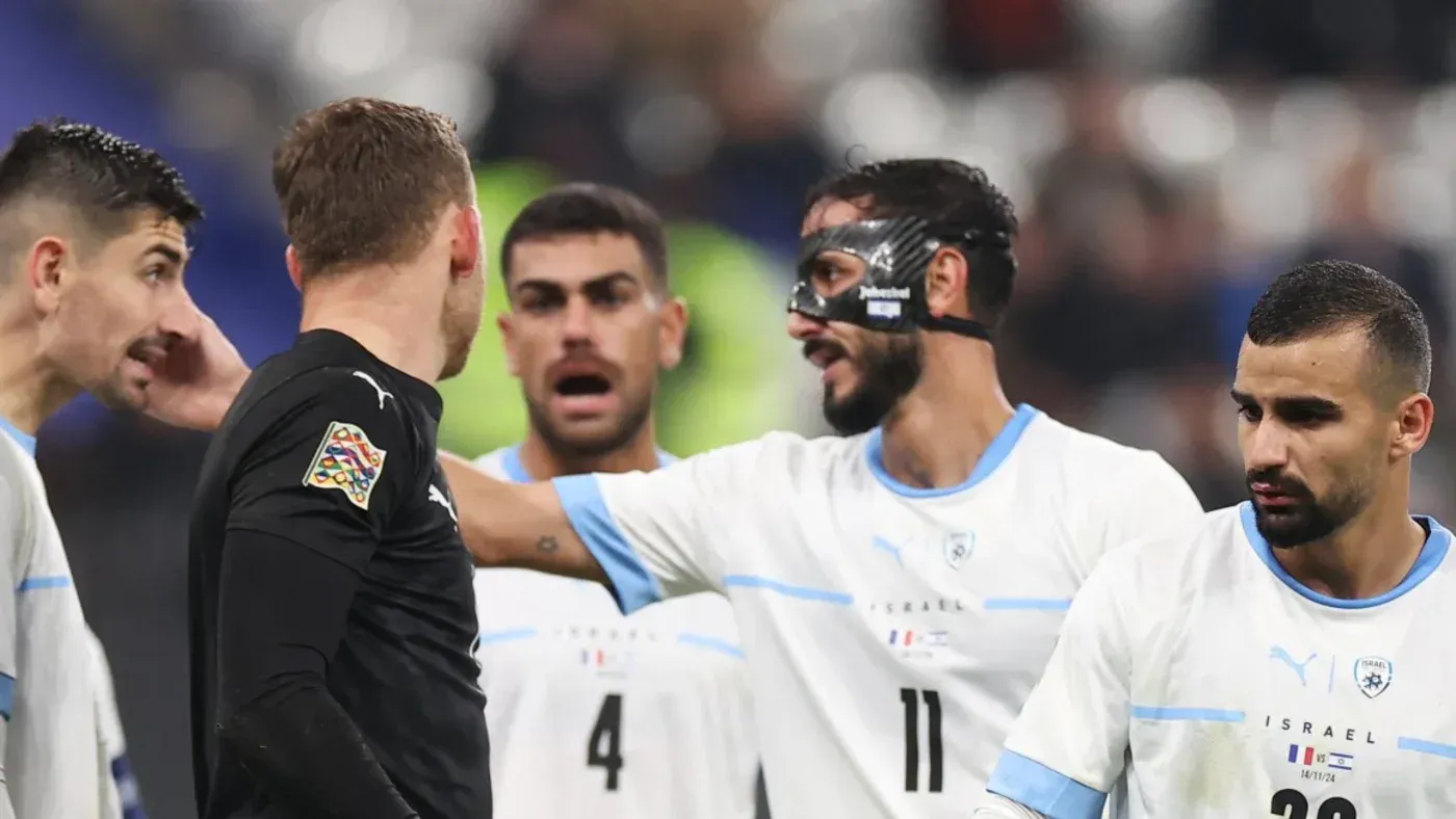 لاعبو المنتخب الإسرائيلي يتحدثون مع الحكم خلال مباراة، مع التركيز على تعبيرات وجههم وتفاعلاتهم، في سياق الجدل حول وضعهم في اليويفا.