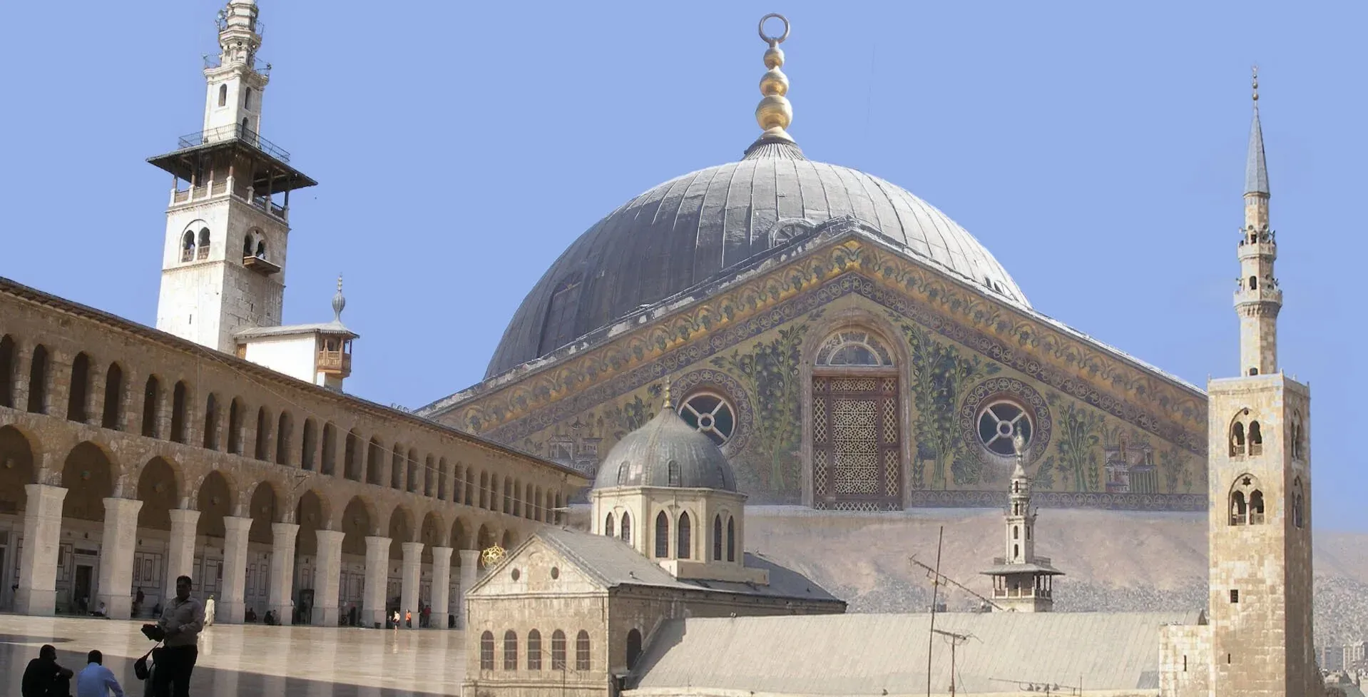 جامع بني أمية في دمشق، يظهر تفاصيل معمارية مميزة، مع مآذن وقبة مزخرفة، يعكس تاريخ المدينة الغني وتنوعها الثقافي.