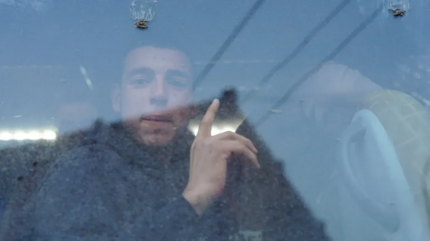 طفل يظهر من نافذة حافلة، يشير بإصبعه، بعد إطلاق سراحه من سجن الأقطان في الرقة، وسط أجواء من الفرح والترحيب.