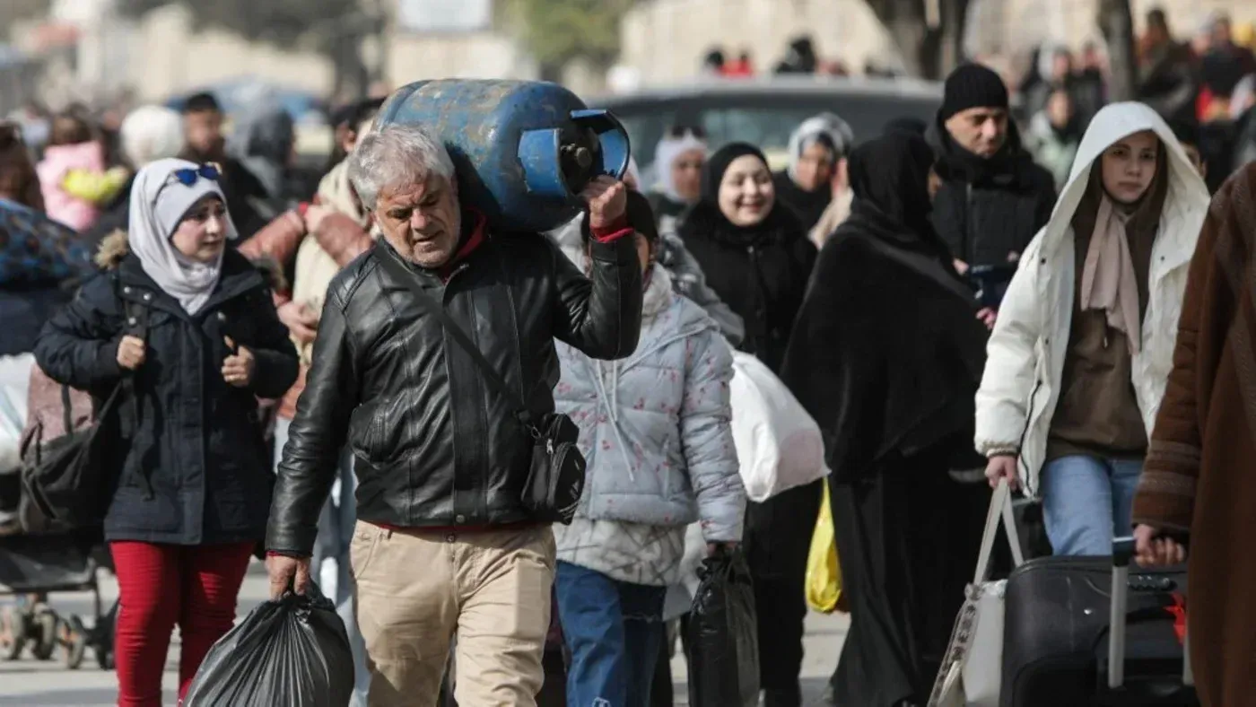 مشهد لمدنيين في حلب يحملون أمتعتهم، مع تصاعد التوترات والعنف في المدينة، حيث يسعون للفرار من الأحياء الكردية.