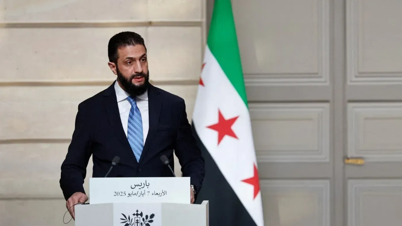 خطاب أحمد الشرع حول رفض الحكم الذاتي في سوريا، مع العلم الوطني السوري خلفه، يعكس التوترات السياسية الحالية.