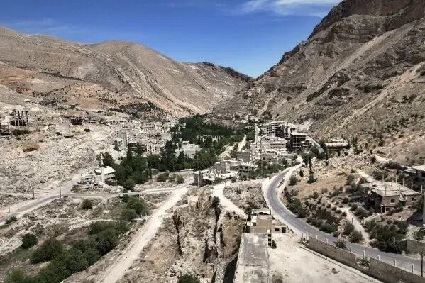 صورة لوادي بردى في سوريا تظهر الجبال الجافة والمنازل المهجورة، تعكس نقص المياه الحاد وتأثير الجفاف على المنطقة.