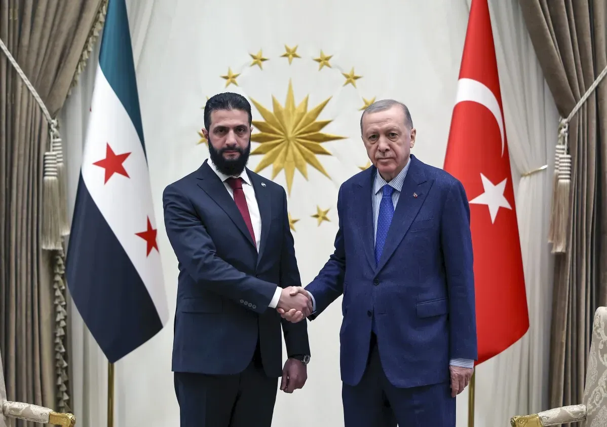 أحمد الشرع، الرئيس السوري المؤقت، يتصافح مع الرئيس التركي رجب طيب أردوغان في القصر الرئاسي بأنقرة، وسط أعلام البلدين.