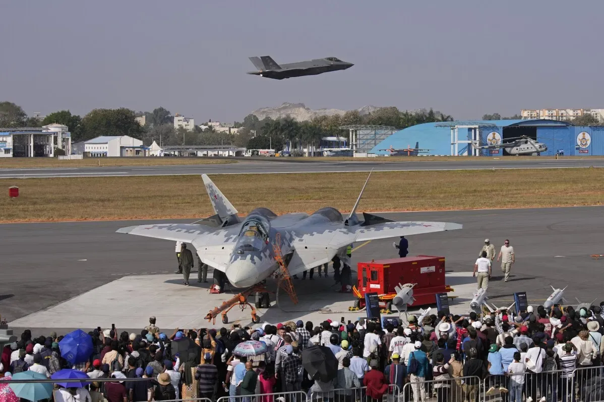 طائرة مقاتلة من طراز F-35 تحلق فوق حشد من الناس في عرض جوي، مع وجود طائرات ومعدات عسكرية في الخلفية، تعكس التعاون الدفاعي بين الهند والولايات المتحدة.