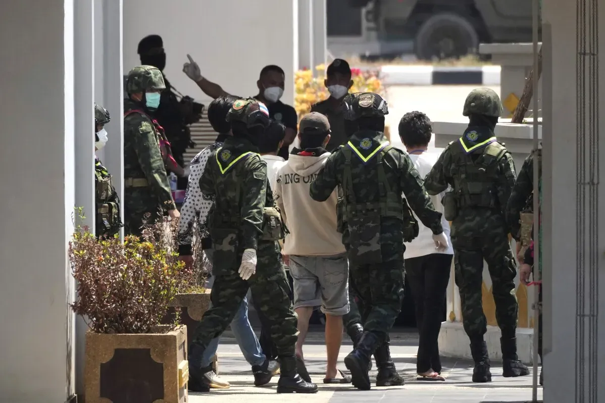 جنود يرتدون زيًا عسكريًا يقودون مجموعة من الأشخاص المحررين من مجمعات الاحتيال في تايلاند، وسط أجواء مشحونة وقلق.