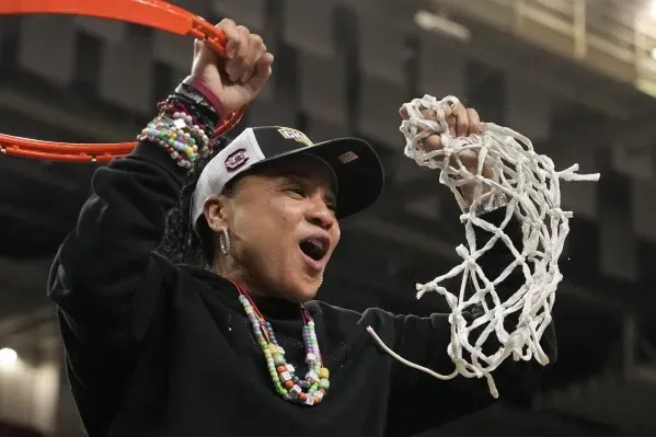 مدربة تحتفل بفوز فريقها في بطولة NCAA، ممسكة بشبكة السلة، تعبيراً عن الفخر والنجاح في الموسم.