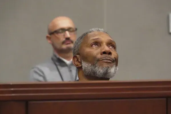 رجل مسن يظهر مشاعر الحزن أثناء جلسة محكمة تتعلق بإطلاق نار جماعي في نورث كارولينا، مع وجود شخص آخر في الخلفية.