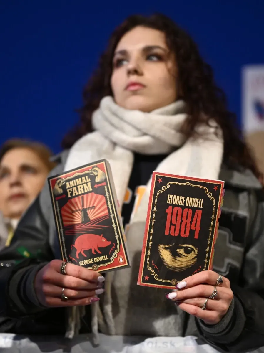 امرأة تحمل كتابين لجورج أورويل، "مزرعة الحيوان" و"1984"، بينما تظهر في خلفية مظاهرة ضد سياسات رئيس الوزراء السلوفاكي.