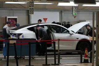سيارة كهربائية من Tesla داخل مصنع في الصين مع فنيين يفحصونها ضمن حملة سحب أكثر من 4 ملايين سيارة بسبب مخاطر مقابض الأبواب.