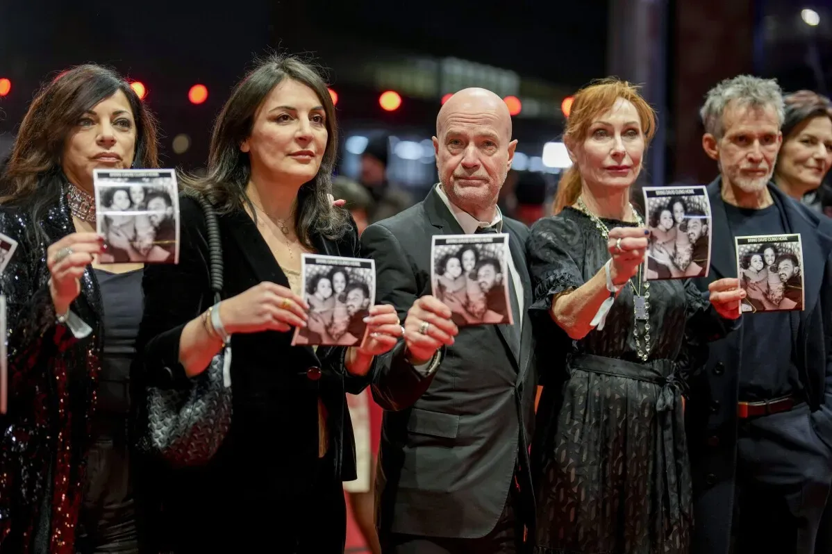 أفراد من صناعة السينما يقفون على السجادة الحمراء في مهرجان برلين السينمائي، يحملون صورًا تتعلق بقضية مهمة.